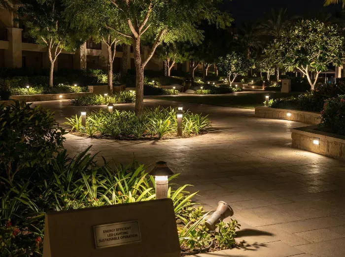 Serene nighttime scene of a stone pathway winding through a lush garden with palm trees, plants, and soft solar-powered lights illuminating the surroundings.