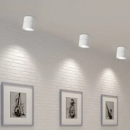 Modern room with white brick walls, three framed abstract black-and-white artworks, and four white cylindrical recessed lights emitting soft illumination from the ceiling.
