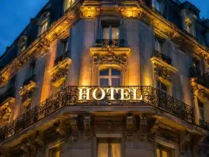 Ornate stone hotel building with balconies and large illuminated HOTEL sign glowing at dusk.