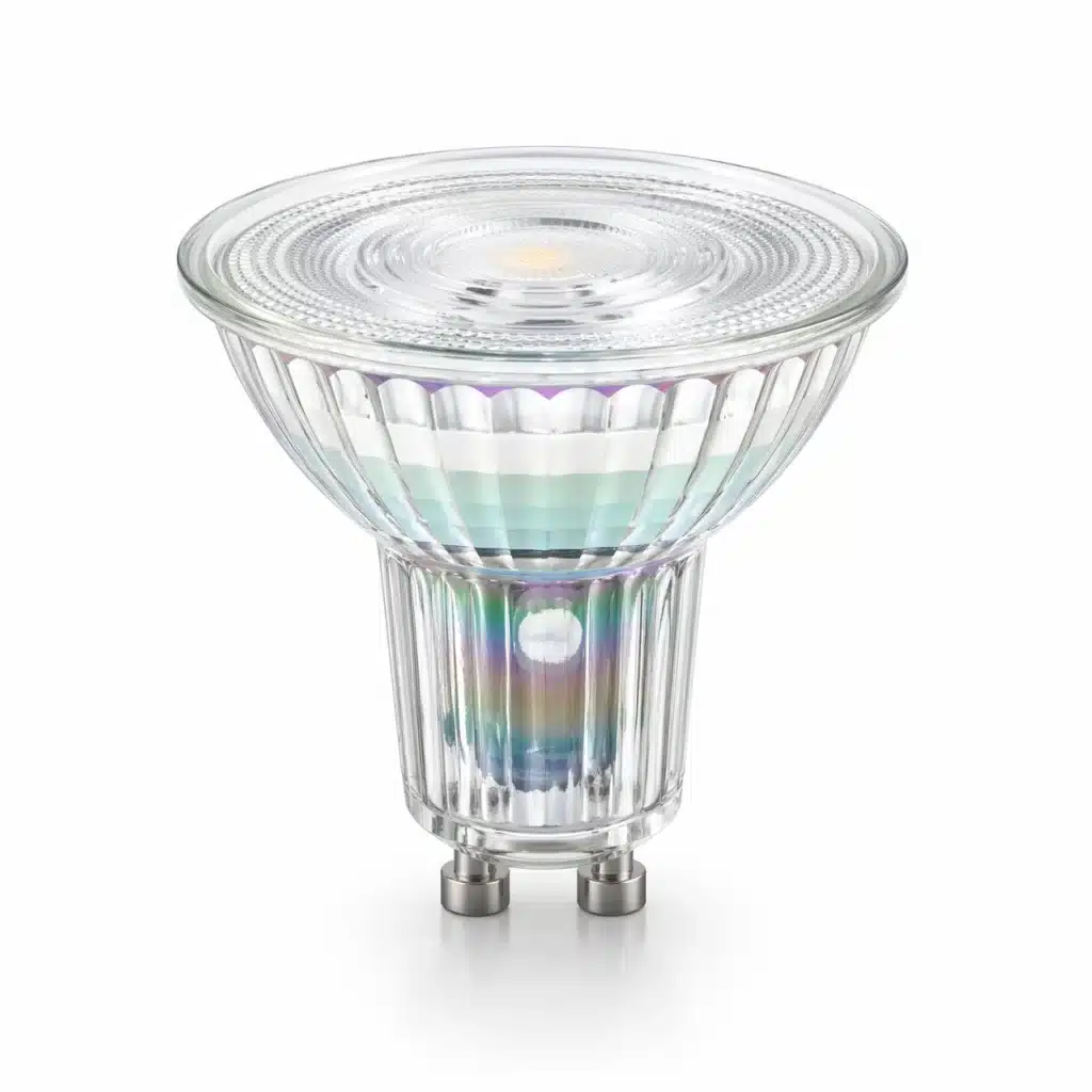 A transparent LED spotlight bulb with colorful iridescent reflections on its faceted glass surface and metal pins.