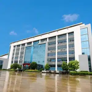 Modern multi-story office building with glass windows and parked cars reflected on wet pavement after rain.