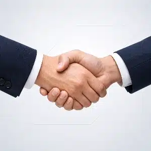 Two individuals wearing navy blue suits engaged in a firm handshake against a light background.