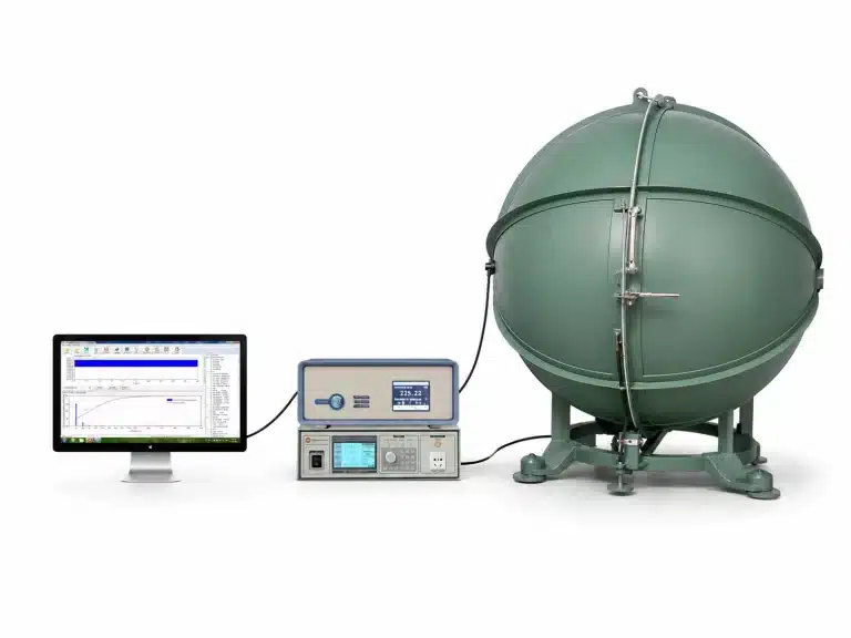 A computer monitor connected to electronic devices and a large green spherical chamber in a laboratory setting.
